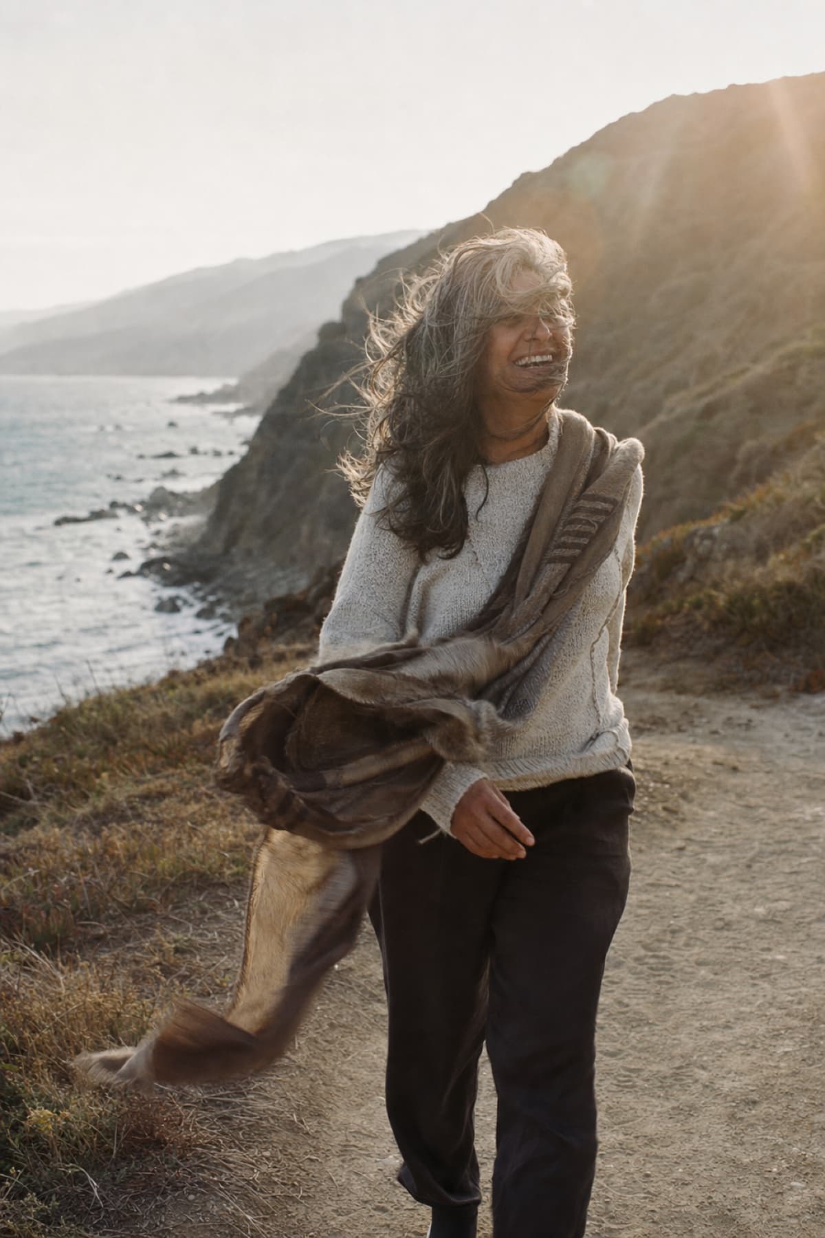 A woman laughing on a windy coastal path in late sun